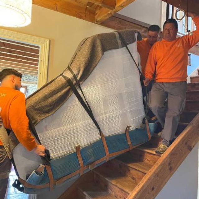 Equipo profesional llevando un piano de cola por escalera complicada para ser trasportado a su lugar de destino