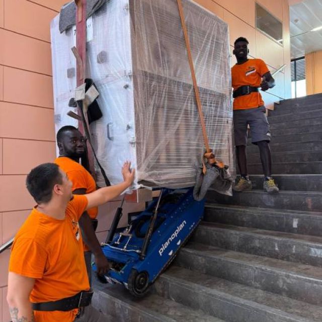 equipo profesional de iprom usando un elevador de pianos para bajar un piano vertical desde un balcón en un segundo piso